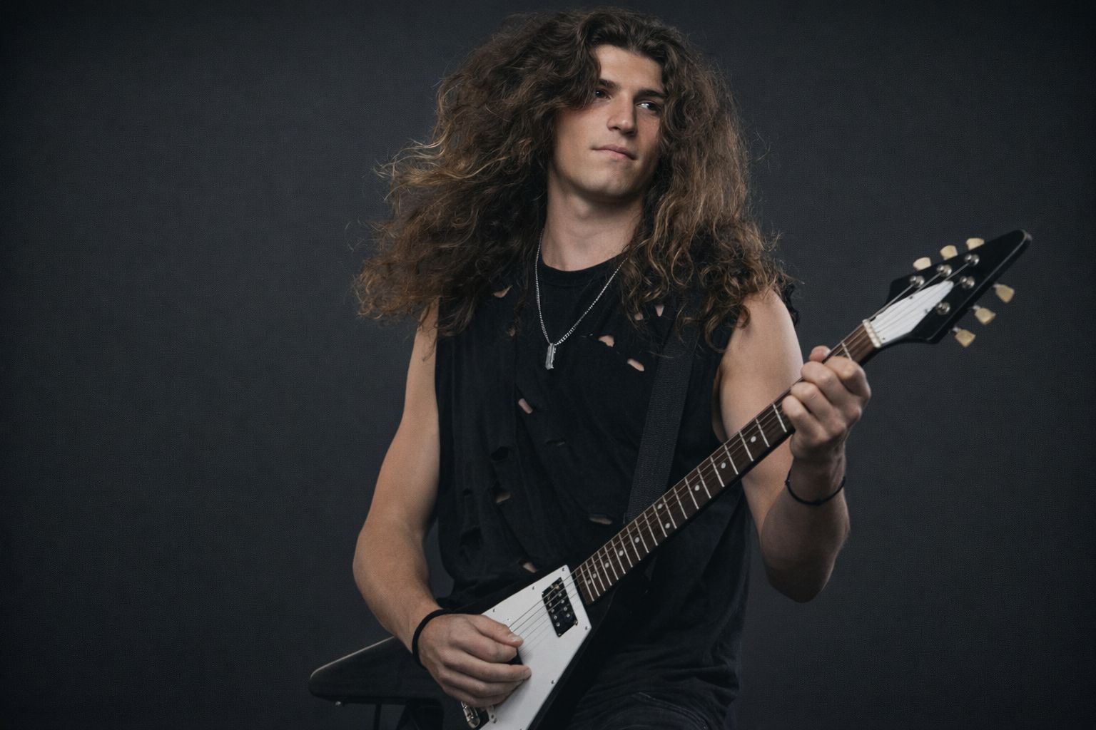 Gitarrist med långt, yvigt hår spelar elgitarr i mörk studio.